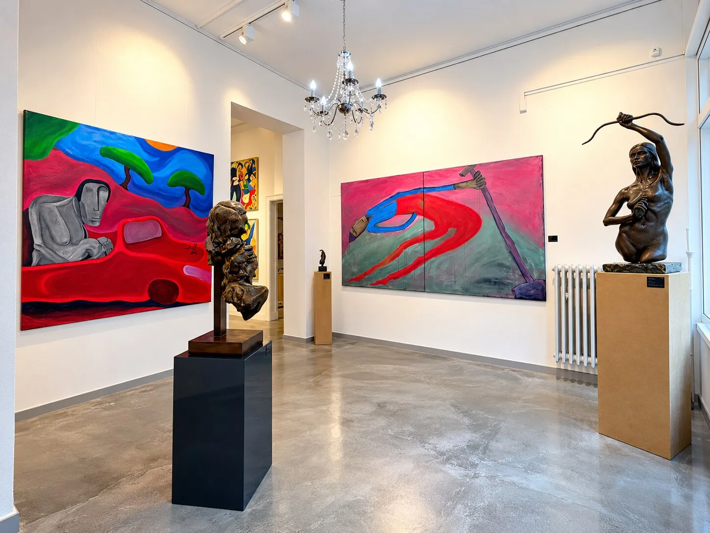 Galerieraum der DNT mit zwei Bronzeskulpturen auf Sockeln, großformatigen farbintensiven Gemälden und einem Kristallkronleuchter.