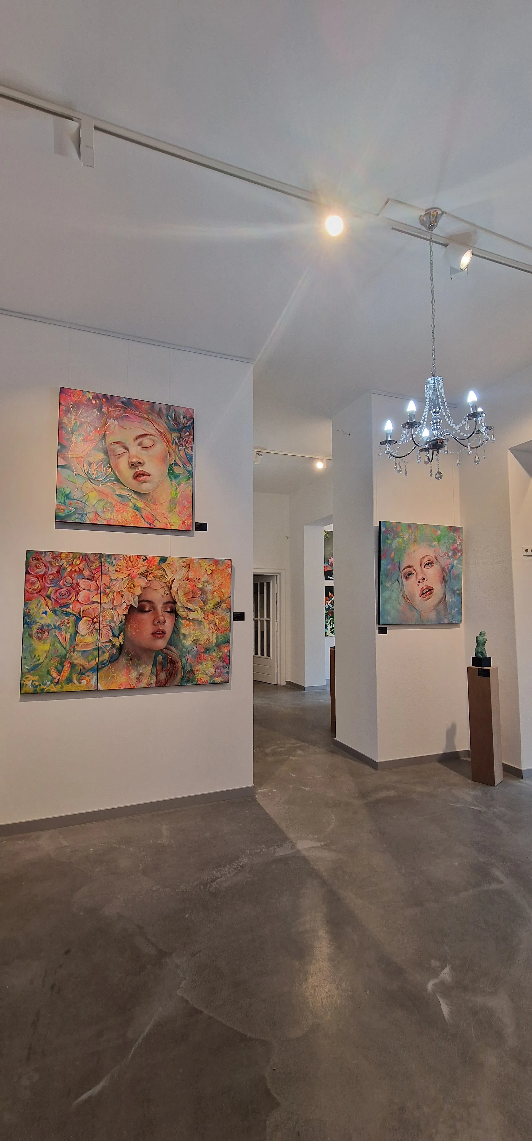 Wandhängung mehrerer farbintensiver Portraitgemälde im DNT-Galerieraum, beleuchtet von einem Kristallkronleuchter.